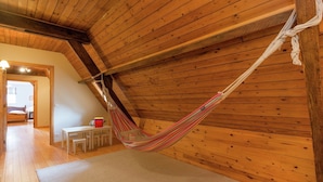 A hammock in a wooden room with a sloped ceiling, a small table, and a chair. - Le Hameau du Château – Elegance and serenity (Libin)