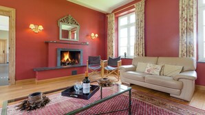 A living room with a fireplace, red walls, a beige sofa, and a glass coffee table. - Le Hameau du Château – Elegance and serenity (Libin)