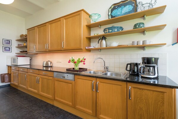 A kitchen with wooden cabinets, a black countertop, a sink, and a coffee maker.