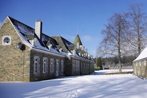 A stone building with multiple chimneys and a snow-covered landscape.