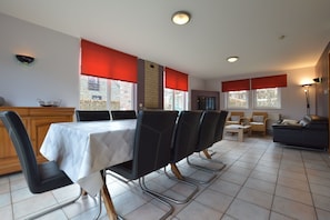 Un coin repas avec une table dressée pour six personnes, entourée de chaises, et un canapé en arrière-plan.