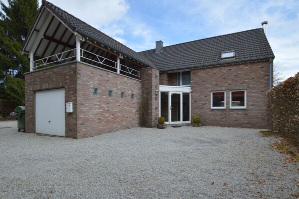Un bâtiment à deux étages, construit en briques, avec un porche couvert, un garage et une allée gravillonnée.
