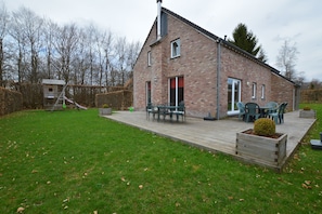Une maison en briques avec une terrasse en bois, un espace salon extérieur et un petit jardin.