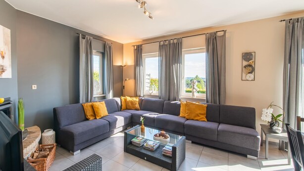 Una sala de estar moderna con un sofá seccional gris, una mesa de centro de vidrio y vistas al exterior.