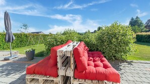 Un patio con una zona de estar con cojines rojos, una mesa de madera y una planta en maceta.