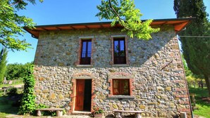 A stone building with two windows and a door, surrounded by greenery.