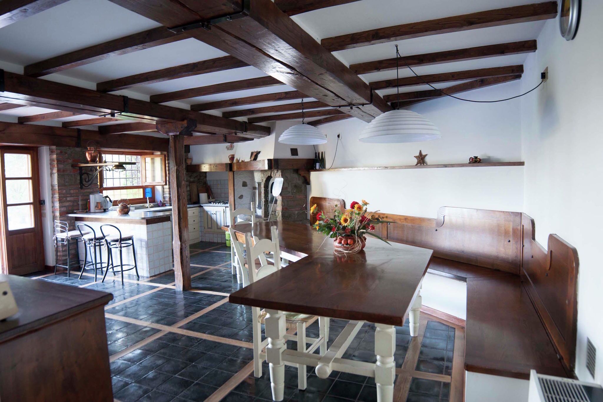 Una cocina rústica con vigas de madera a la vista, una isla central con sillas y una mesa de comedor con un jarrón de flores.
