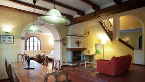 A dining area with a wooden table and chairs, a red sofa, and a fireplace. - Villa in Casentino with Pool & Castle Views (Stia)