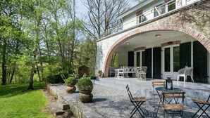 A covered patio with outdoor furniture, a brick archway, and a view of the surrounding greenery. - Holiday Home in Dalhem with Private Sauna (Aubel)