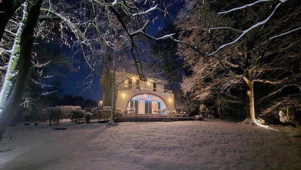A snow-covered courtyard with a building featuring a large arched entrance and illuminated windows. - Holiday Home in Dalhem with Private Sauna (Aubel)