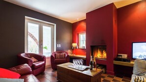 A living room with a fireplace, leather sofas, a coffee table, and a television. - Holiday Home in Dalhem with Private Sauna (Aubel)