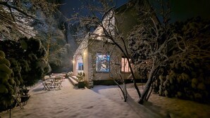 A snow-covered garden with a building, outdoor seating, and a lit window. - Holiday Home in Dalhem with Private Sauna (Aubel)