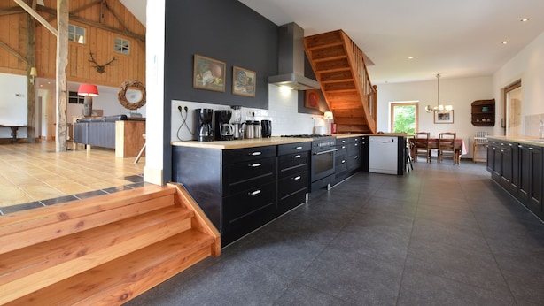 A spacious kitchen with a central island, wooden staircase, and a dining area with a table and chairs.