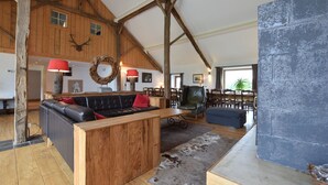 A rustic interior with wooden beams, a black leather sofa, a wooden coffee table, and a stone fireplace.