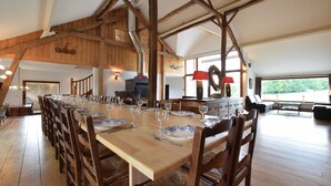 A dining area with a long wooden table set for a meal, wooden beams on the ceiling, and a fireplace.