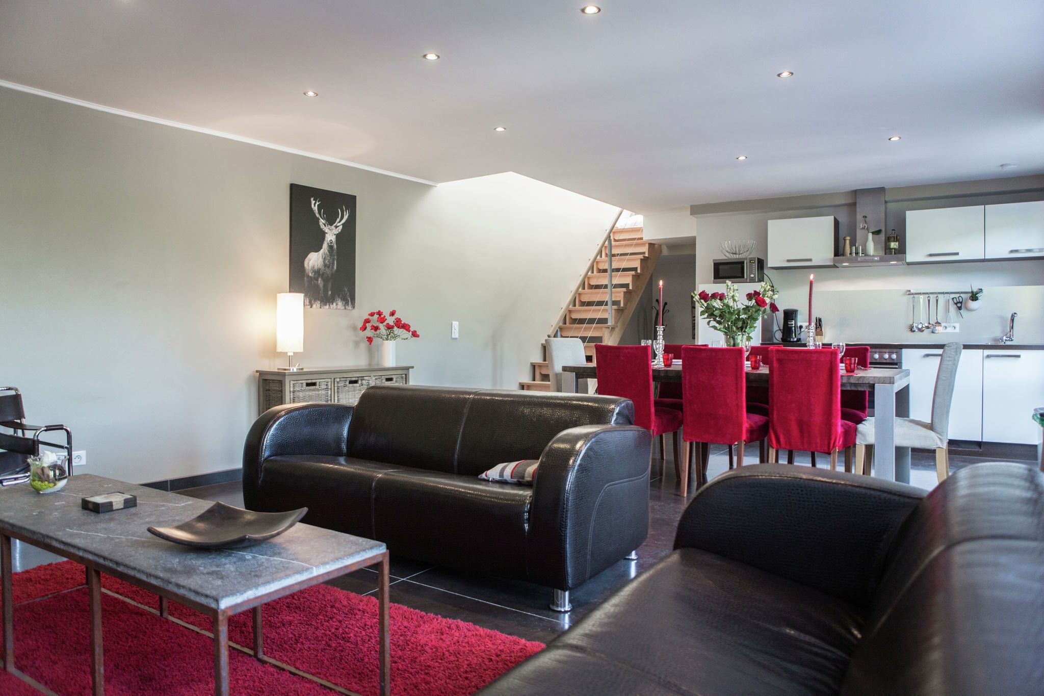 Ein modernes Wohnzimmer mit einer schwarzen Ledersofa, einer Essecke mit roten Stühlen und einer Küche im Hintergrund.