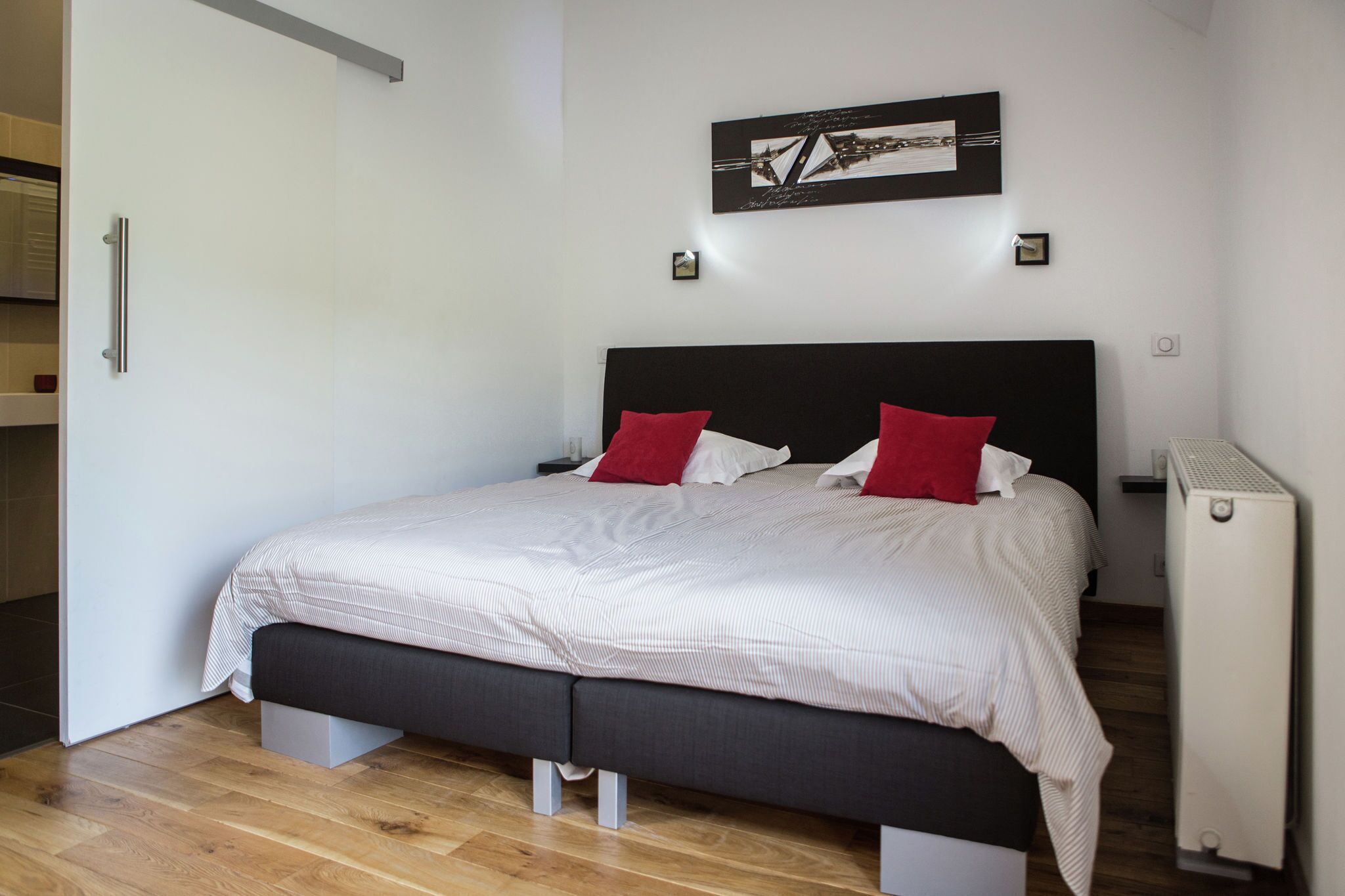 A modern bedroom with a large bed, a black headboard, and a red and white striped bedspread.