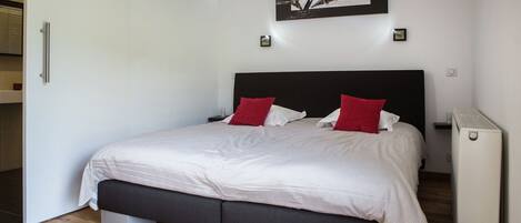 A modern bedroom with a large bed, a black headboard, and a red and white striped bedspread.