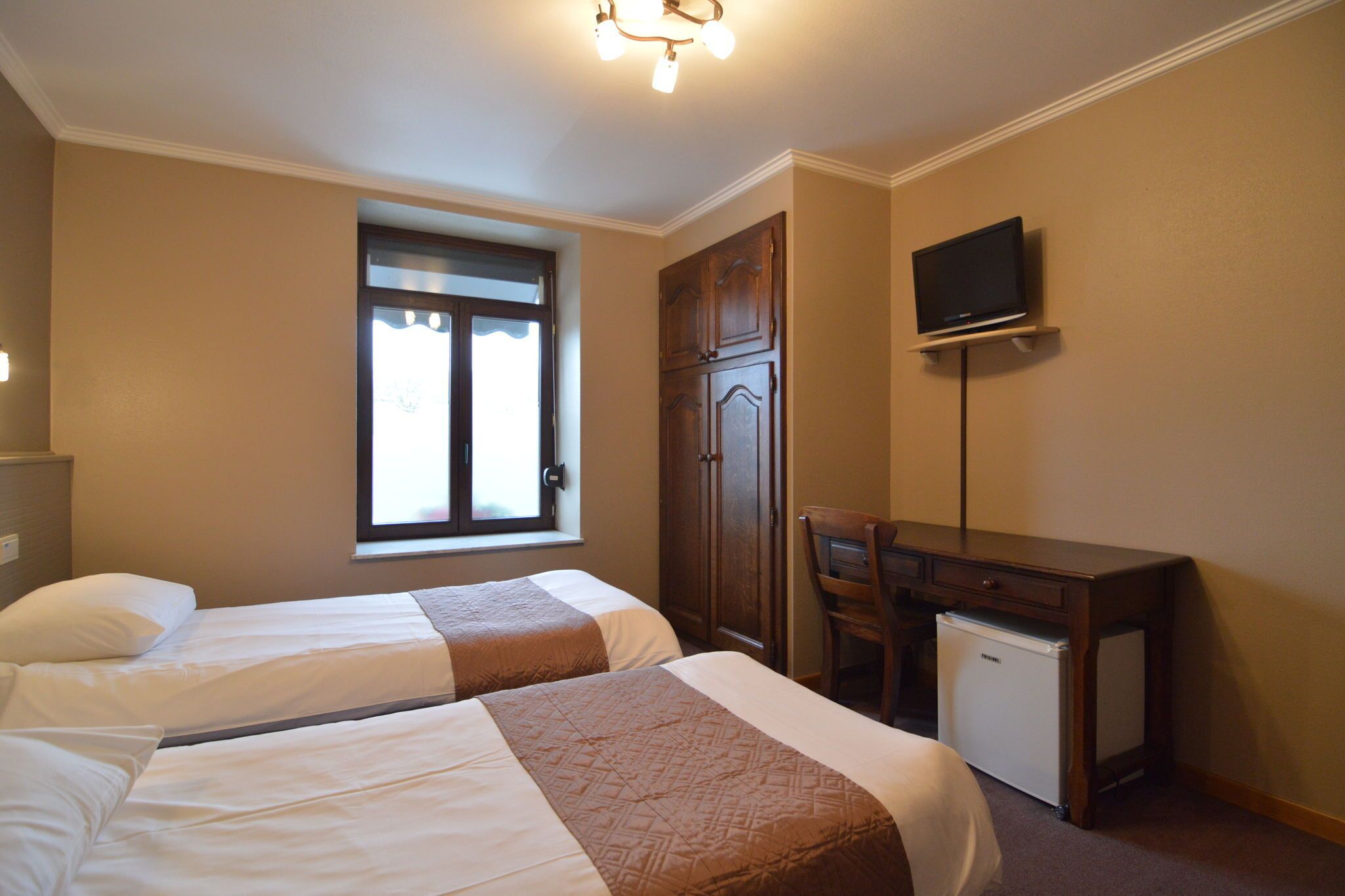 A hotel room with two beds, a desk, a television, and a small refrigerator.