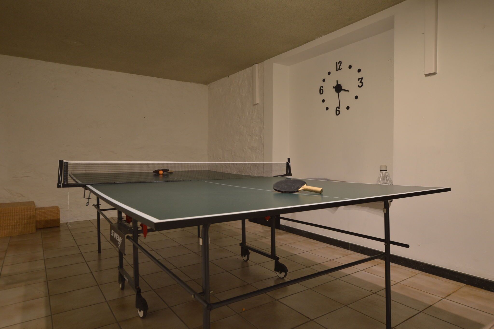 A ping pong table with a net in a room with a clock on the wall.