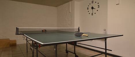 A ping pong table with a net in a room with a clock on the wall.