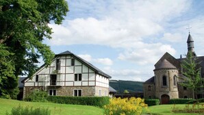 A traditional half-timbered house with a stone church in the background. - Holiday Home in Stoumont near Spa Resort (Stoumont)