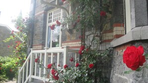Un edificio de piedra con un porche blanco y rosales rojos trepando por las paredes.