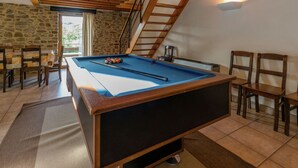 A pool table in a room with stone walls, wooden ceiling beams, and a staircase.
