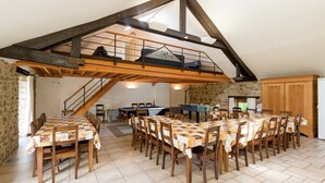 A spacious dining area with a high ceiling and exposed wooden beams, a stone wall, and a billiards table.