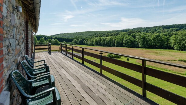 A wooden deck with benches, overlooking a green field and forested hills.