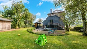 Een huis met een ruime achtertuin, een speelruimte en een overdekt terras.