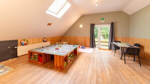 Een ruime kamer met een grote houten tafel, stoelen en een speelgedeelte voor kinderen.