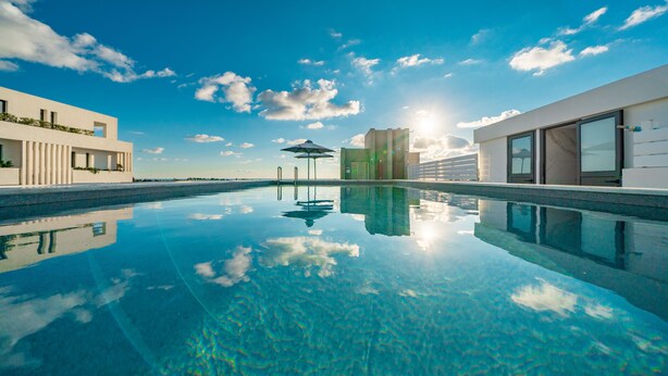 Une piscine aux eaux cristallines, avec un bâtiment moderne d’un côté et un ciel dégagé au-dessus.