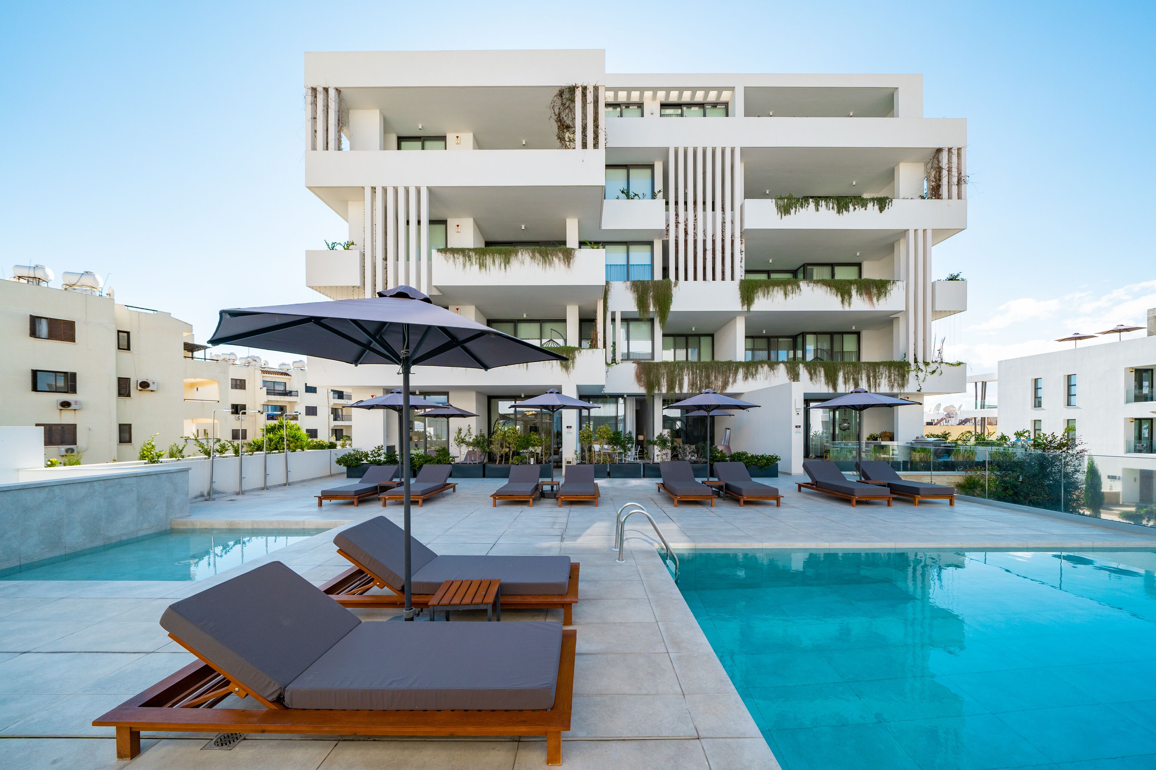 A rooftop pool area with lounge chairs and umbrellas, surrounded by modern buildings.