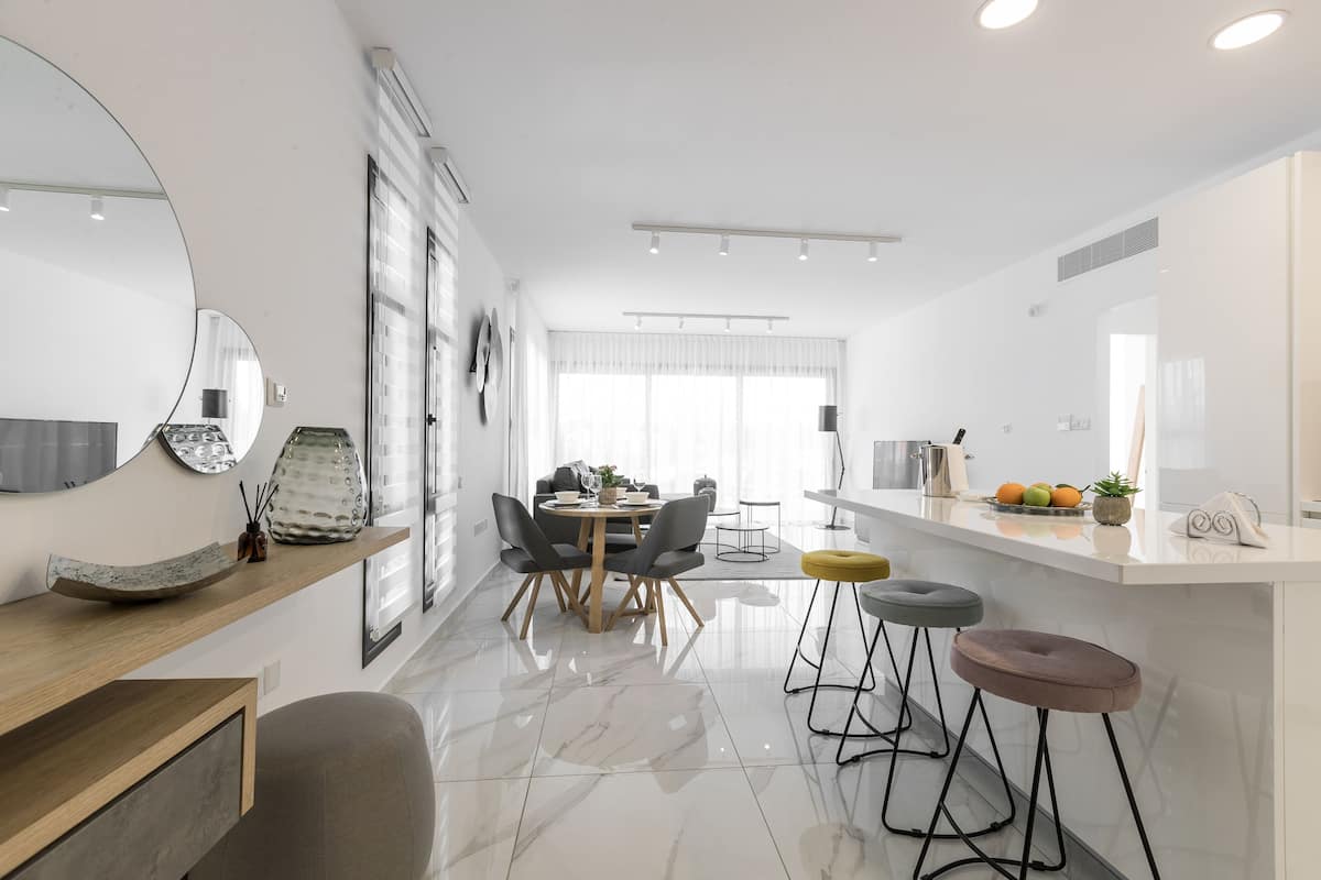 Una cocina moderna con encimera blanca, un comedor con mesa redonda y sillas, y una barra con taburetes.