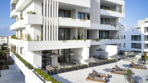 Un immeuble moderne à plusieurs étages, doté de balcons, d’un espace extérieur aménagé pour s’asseoir et d’une piscine.