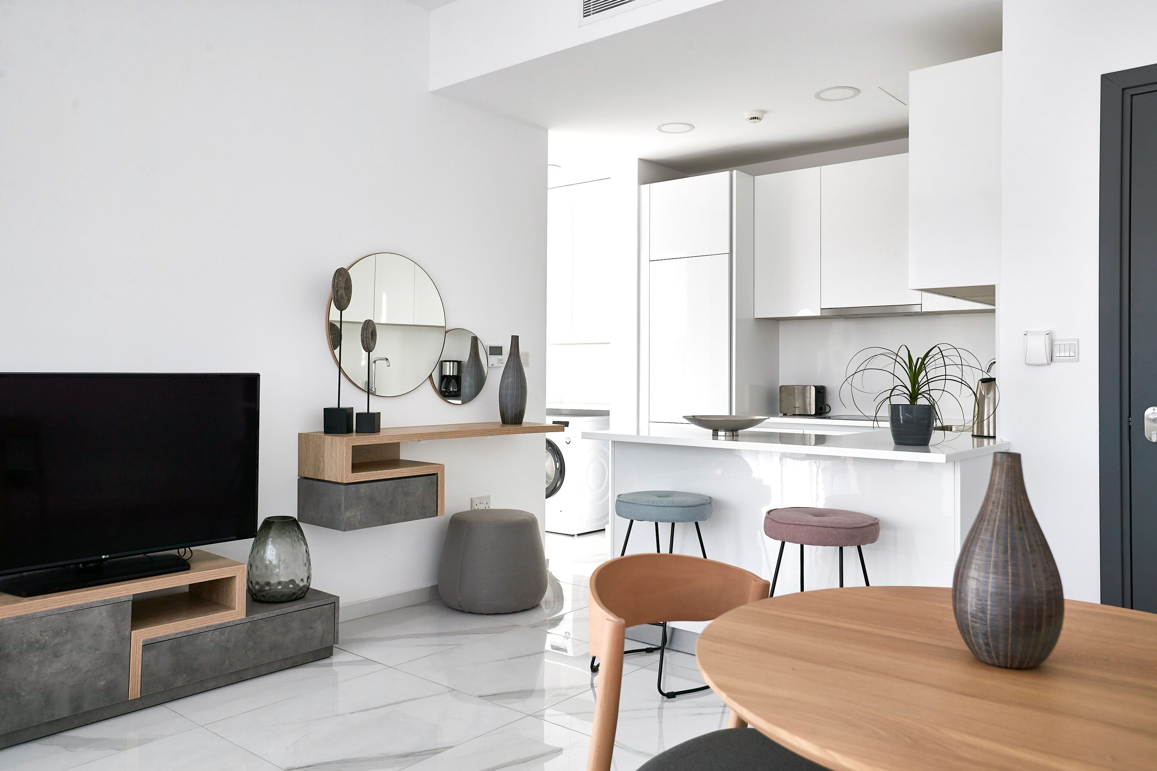 Un salon moderne avec un téléviseur à écran plat, une table à manger et un coin cuisine à l’arrière-plan.