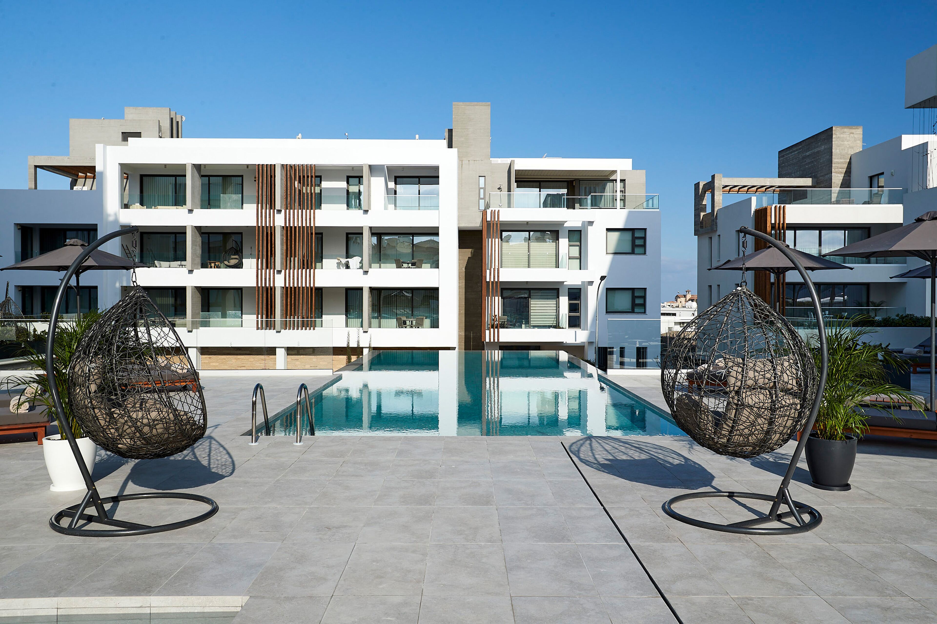 Un bâtiment moderne doté d’une piscine sur le toit, de deux fauteuils suspendus et de plantes en pot.