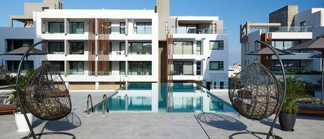 Un bâtiment moderne doté d’une piscine sur le toit, de deux fauteuils suspendus et de plantes en pot.