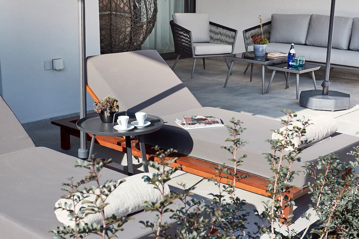 Un área de estar moderna al aire libre, con un sofá, dos sillones, una mesa redonda y una mesita con una planta y una revista.