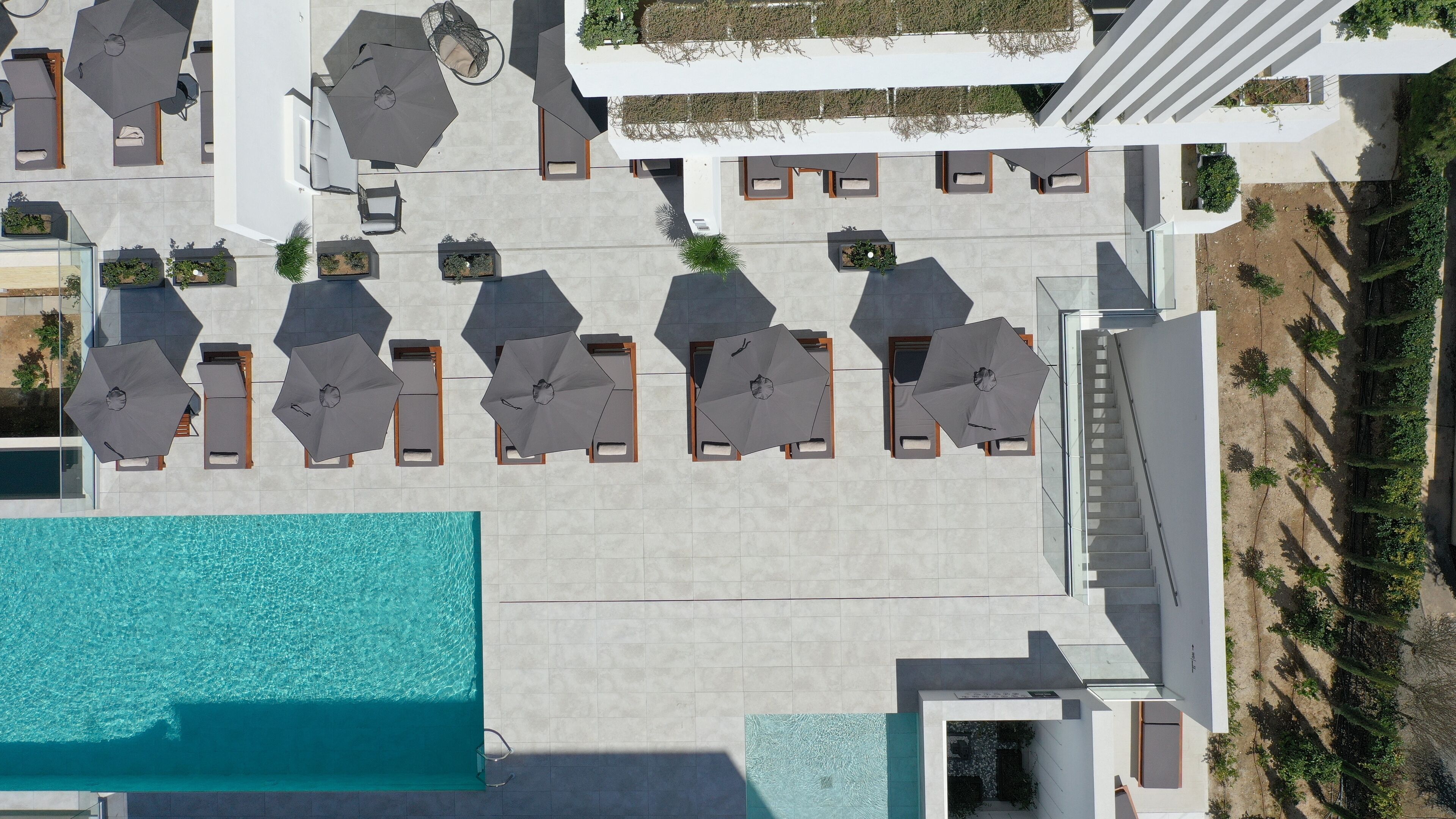 Vue aérienne d’un hôtel doté d’une piscine, de plusieurs espaces de détente avec des parasols et d’un escalier menant à un niveau supérieur.
