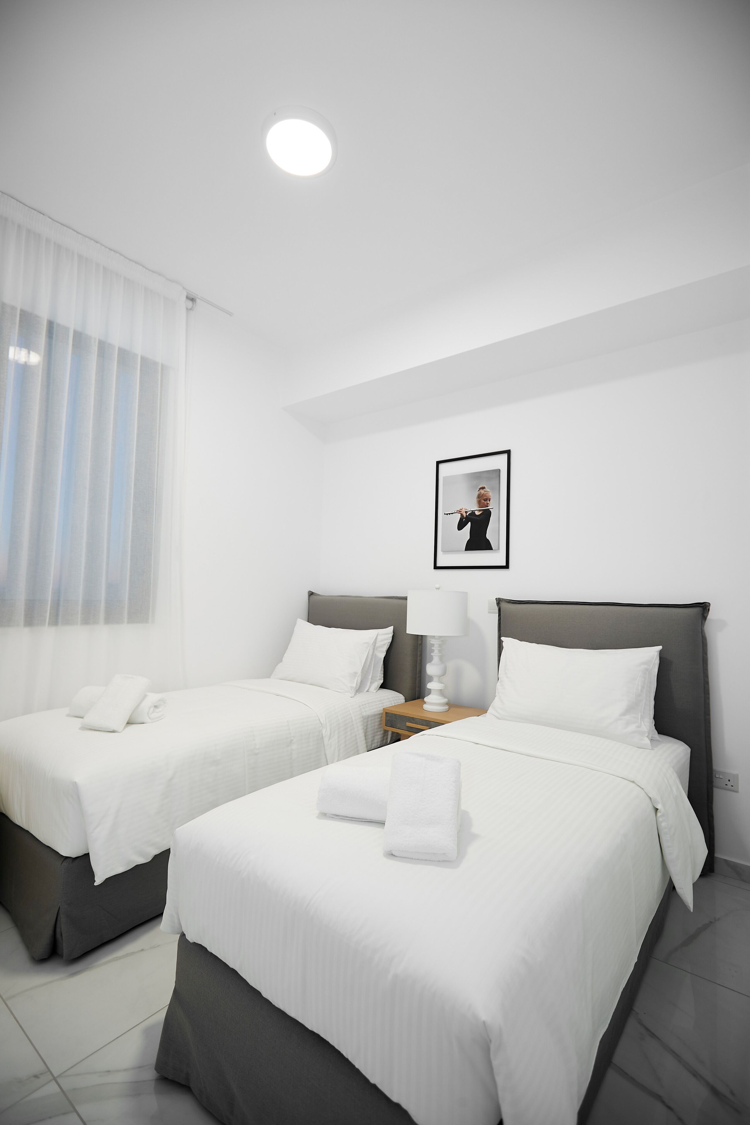 A hotel room with two beds, a nightstand, a lamp, and a framed picture on the wall.