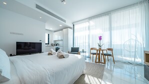 Une chambre d  ’hôtel moderne dotée d’un grand lit, d’un téléviseur à écran plat, d’un coin repas avec une table et des chaises, et d’une grande fenêtre avec des rideaux légers.