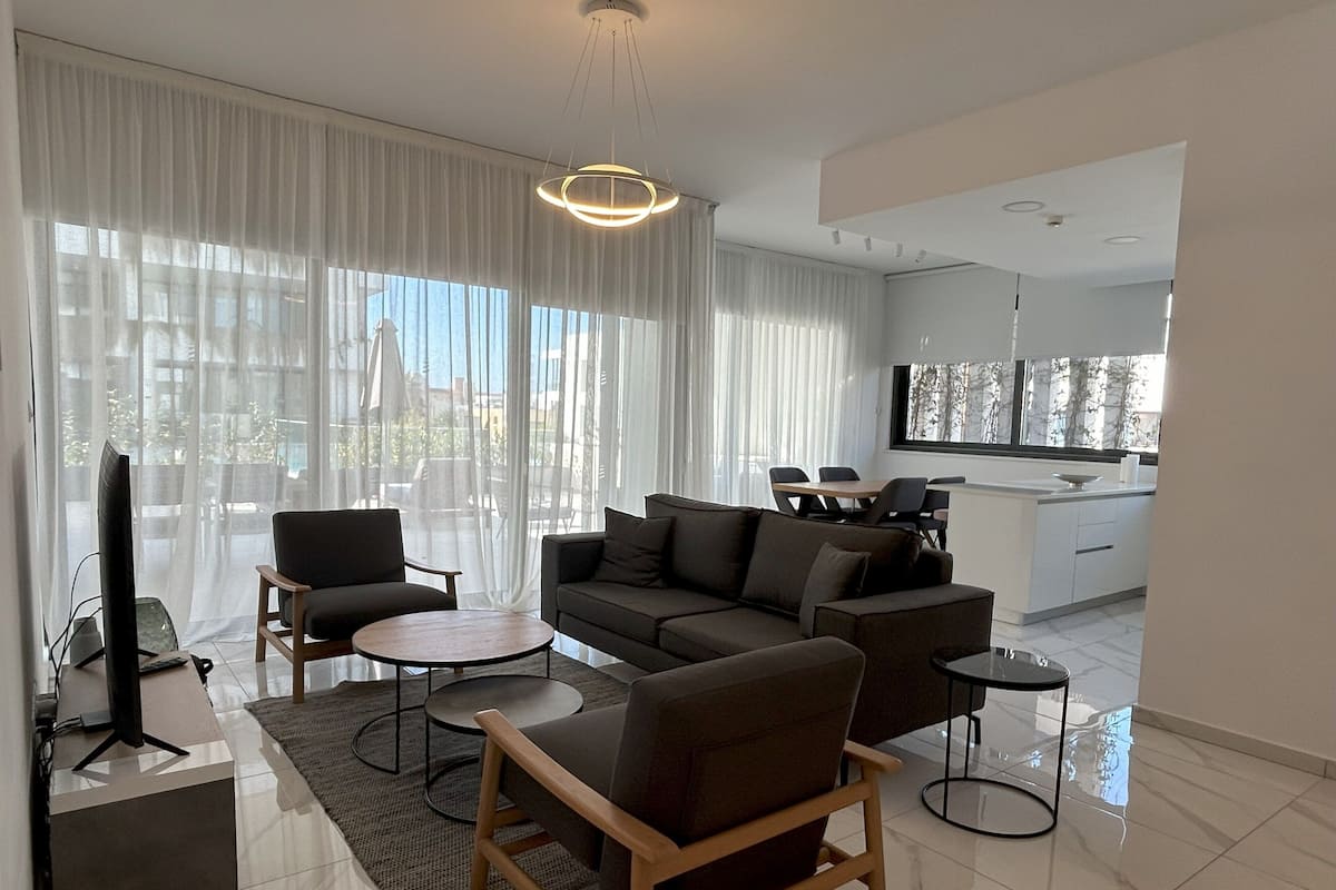 Una sala de estar moderna con un sofá, sillas, un televisor y un comedor con una mesa y sillas.