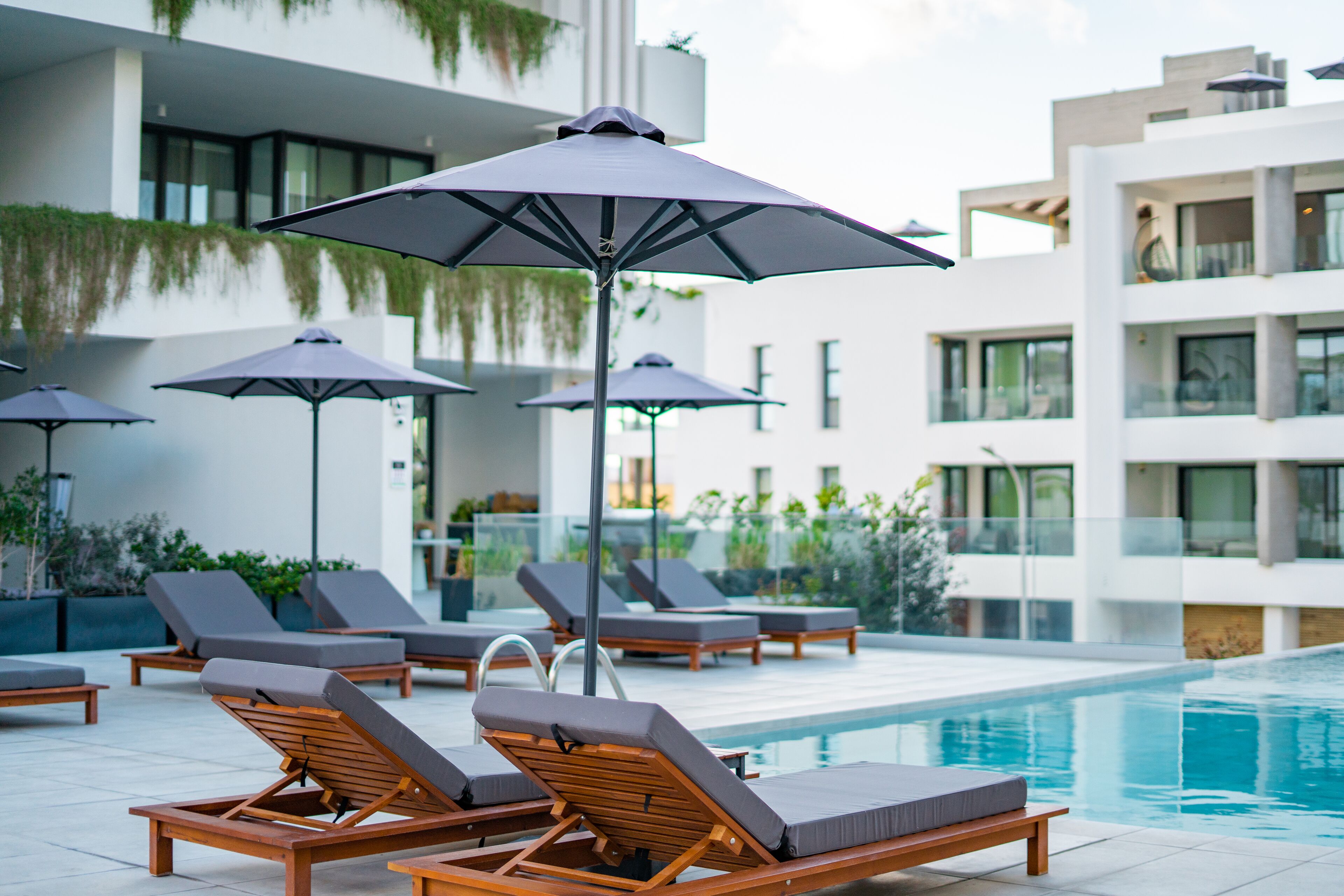 A poolside area with lounge chairs and umbrellas, a modern building with balconies, and a clear pool.