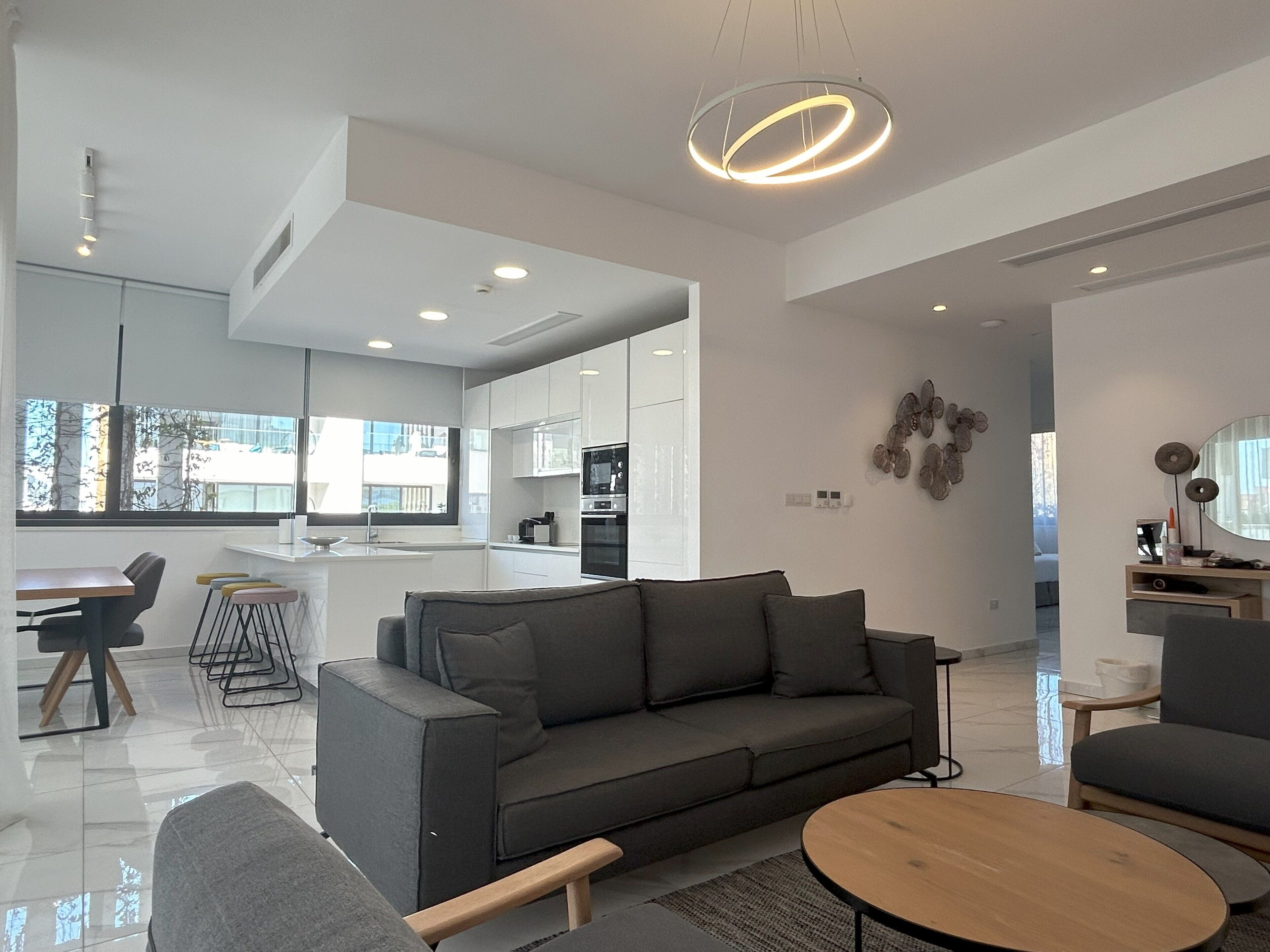 A modern living room with a grey sofa, a round coffee table, and a dining area with a bar.