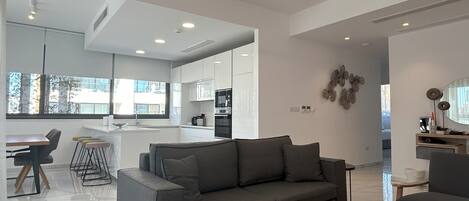 A modern living room with a grey sofa, a round coffee table, and a dining area with a bar.