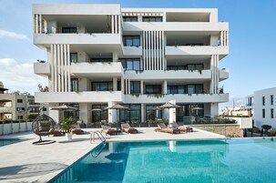 A modern multi-story building with a rooftop pool area, including lounge chairs, umbrellas, and a hanging chair.