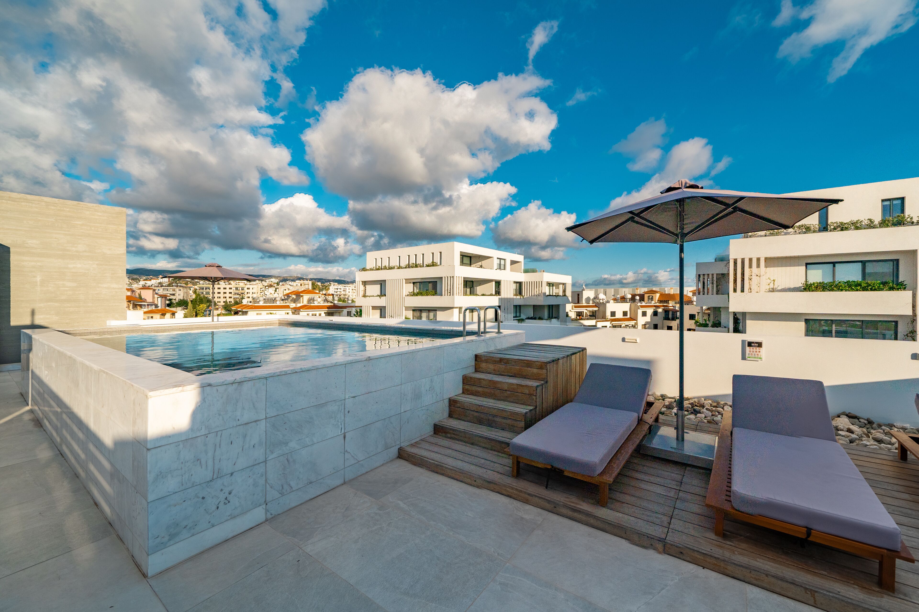 A rooftop pool area with lounge chairs and a wooden deck.
