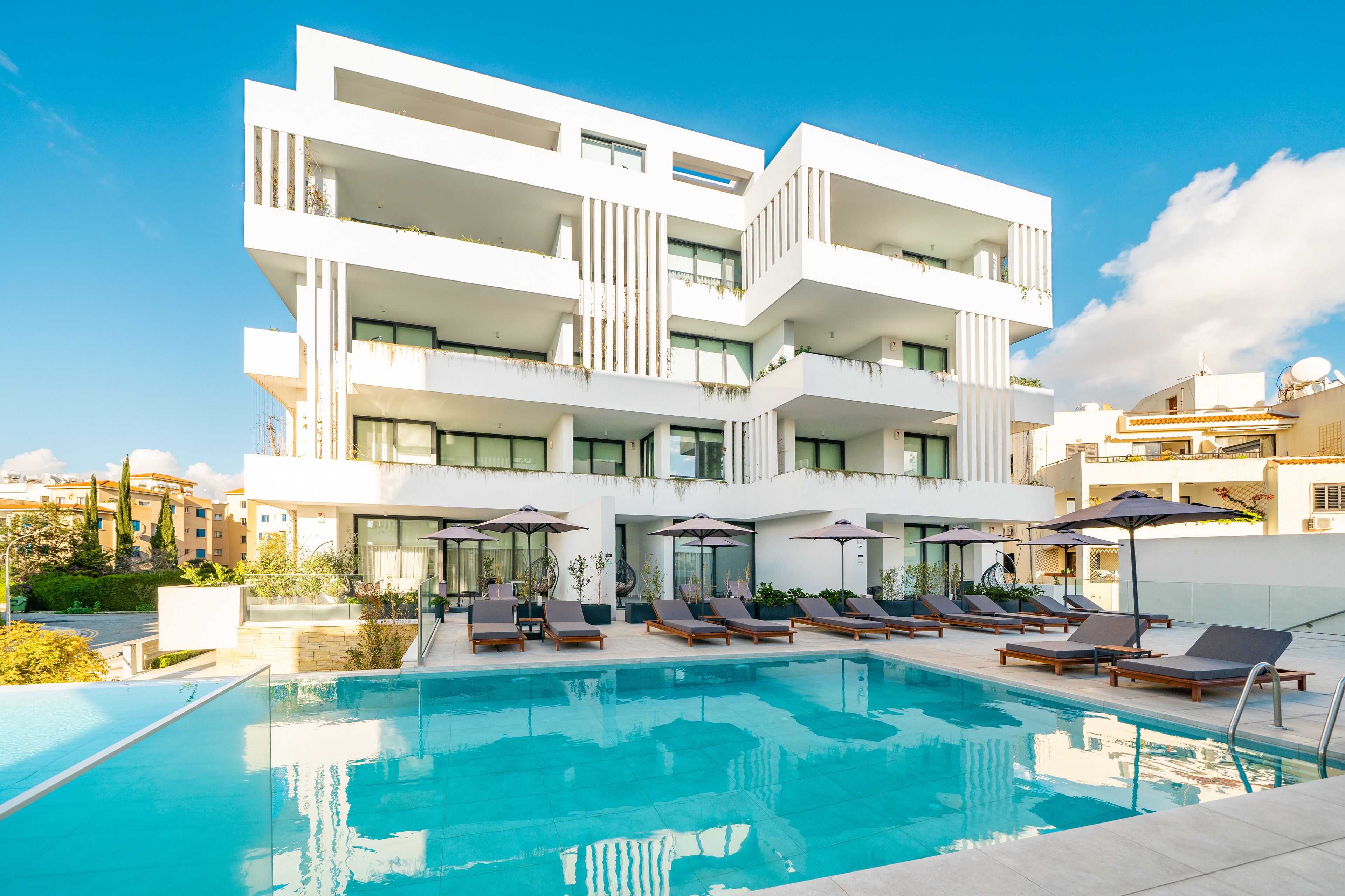 A modern hotel with a pool area, multiple balconies, and lounge chairs.